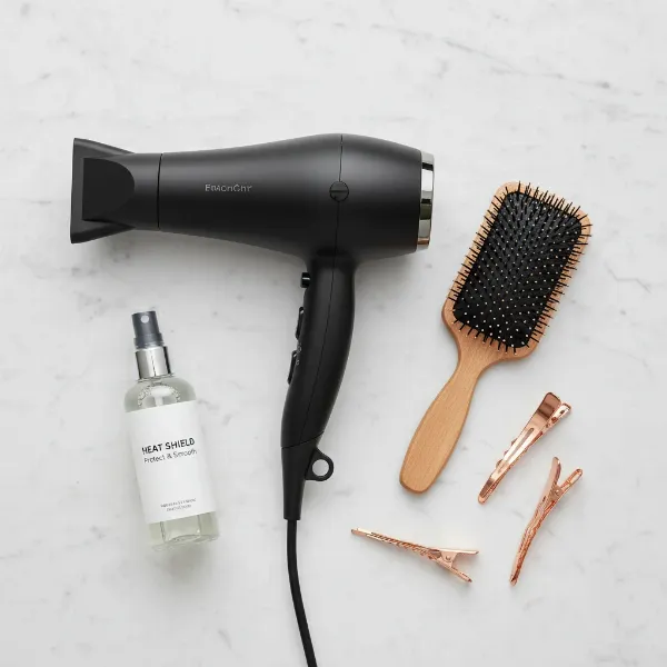 A collection of essential tools for blow drying bangs flat: a hair dryer with a concentrator nozzle, a paddle brush, hair clips, and a heat protectant spray.